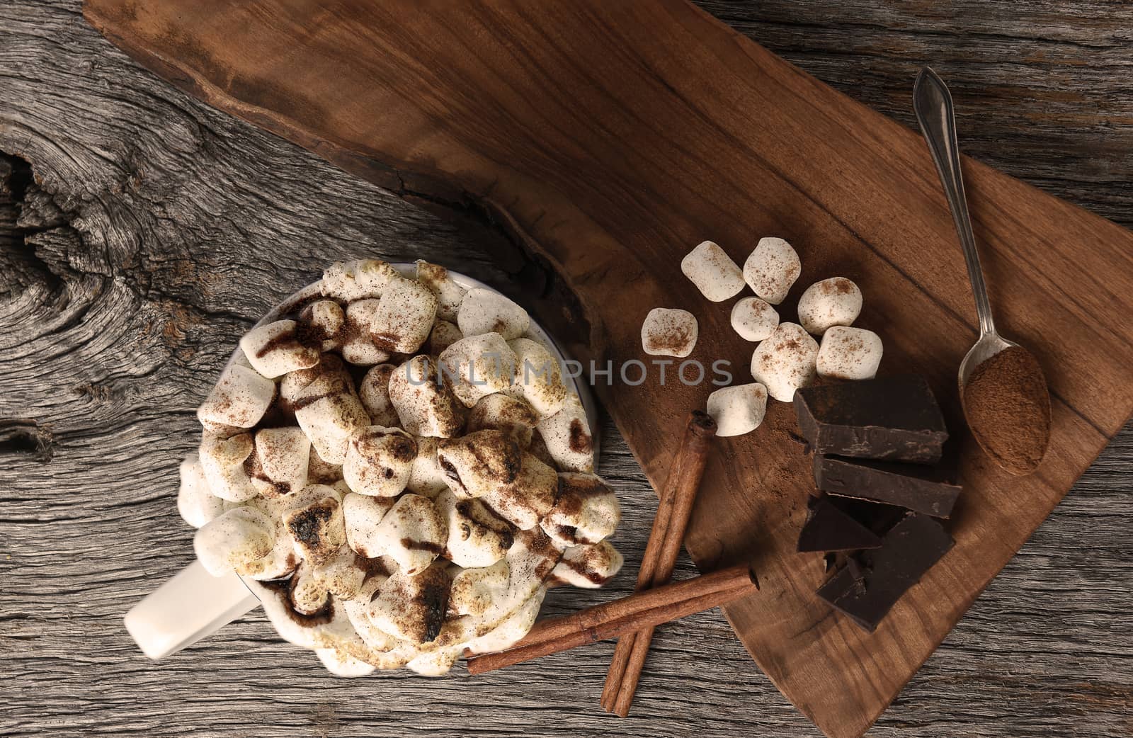 Overhead shot of a mug of hot cocoa with toasted marshmallows next to a cutting board with chocolate chunks and cinnamon sticks. 