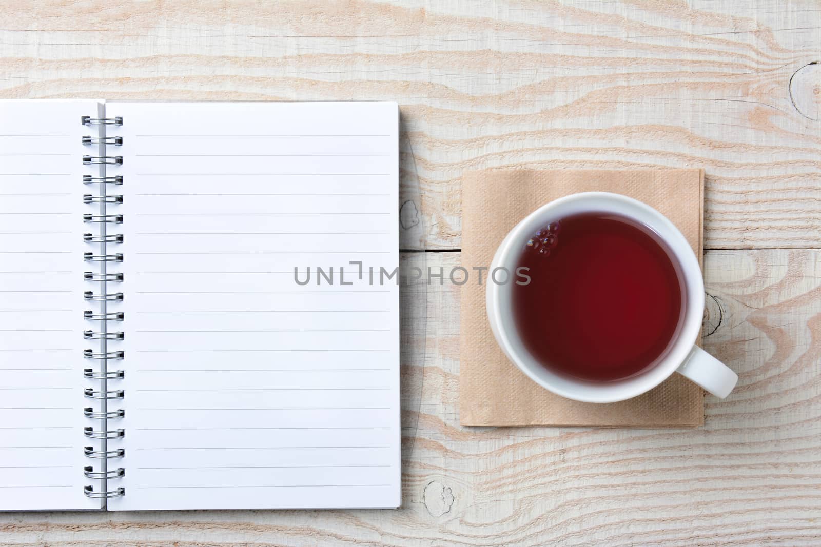 Closeup of an open notebook and a cup of hot tea on a rustic white wood table. High angle shot in horizontal format.