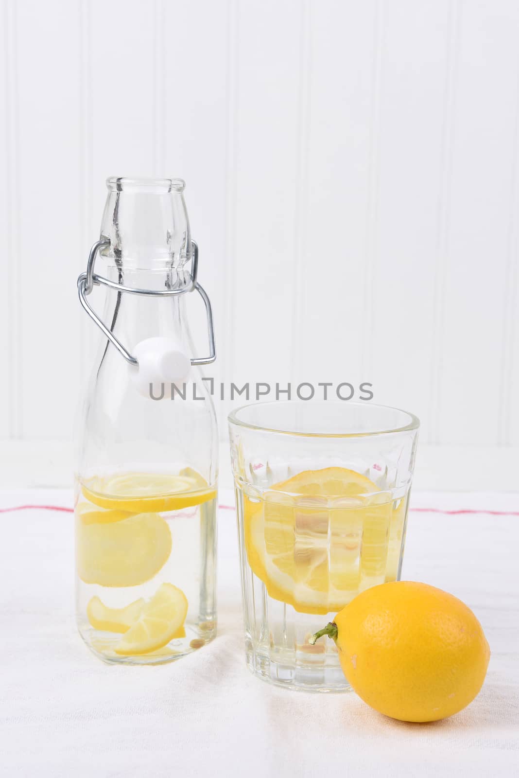 A swing top bottle and glass of lemon water on a linen towel in an all white set.