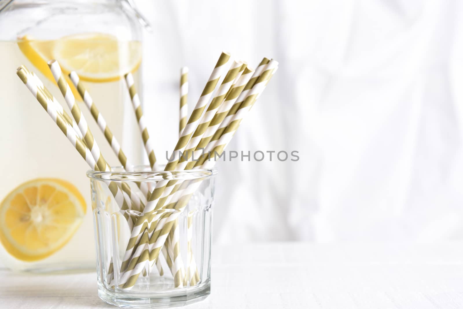 Summer Lemonade Still Life: A lemonade pitcher with a glass of drinking straws in front of a kitchen window. Horizontal format with copy space. Focus is on straws.