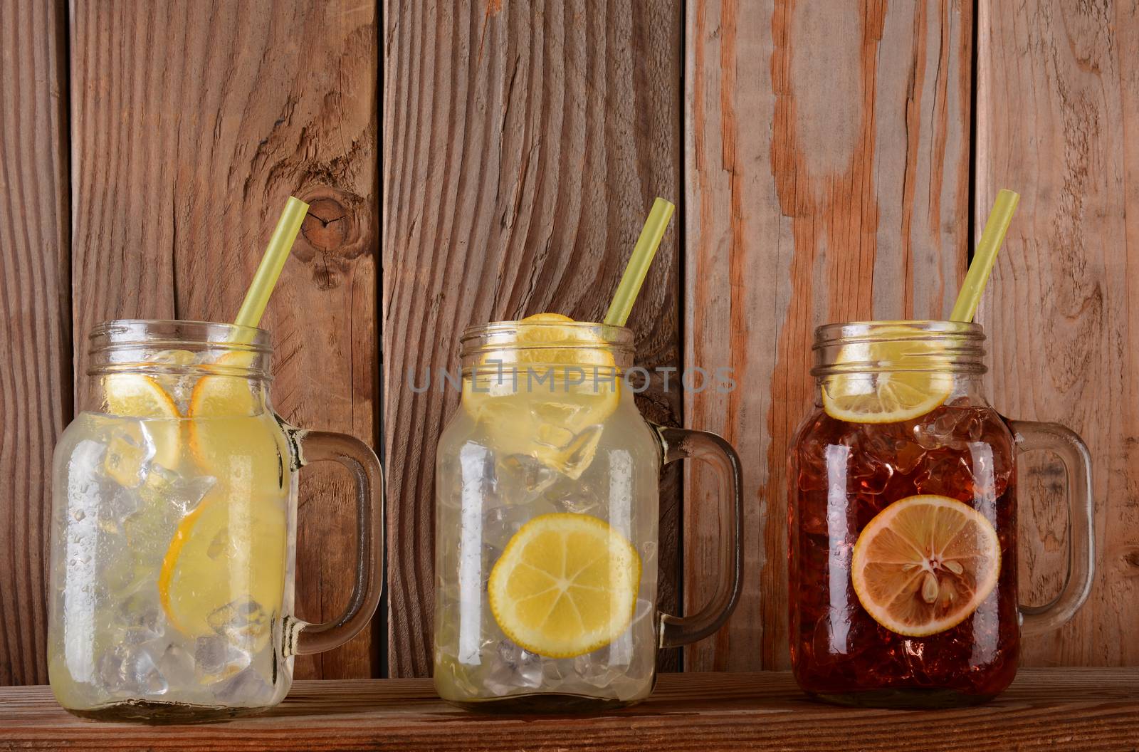 Glasses of lemonade and fruit Juice on a rustic kitchen ledge. The mason jar style glasses have handles and drinking straws. 