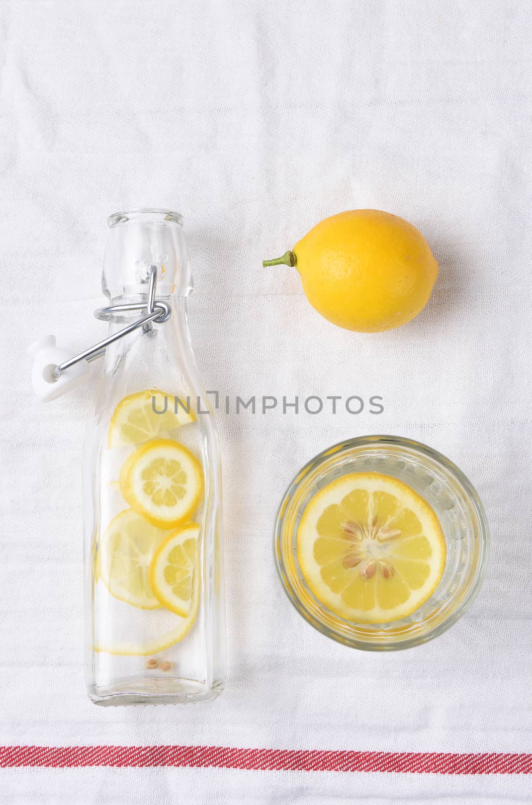 Top view of a glass of lemon water next to a swing bottle and whole piece of fruit.