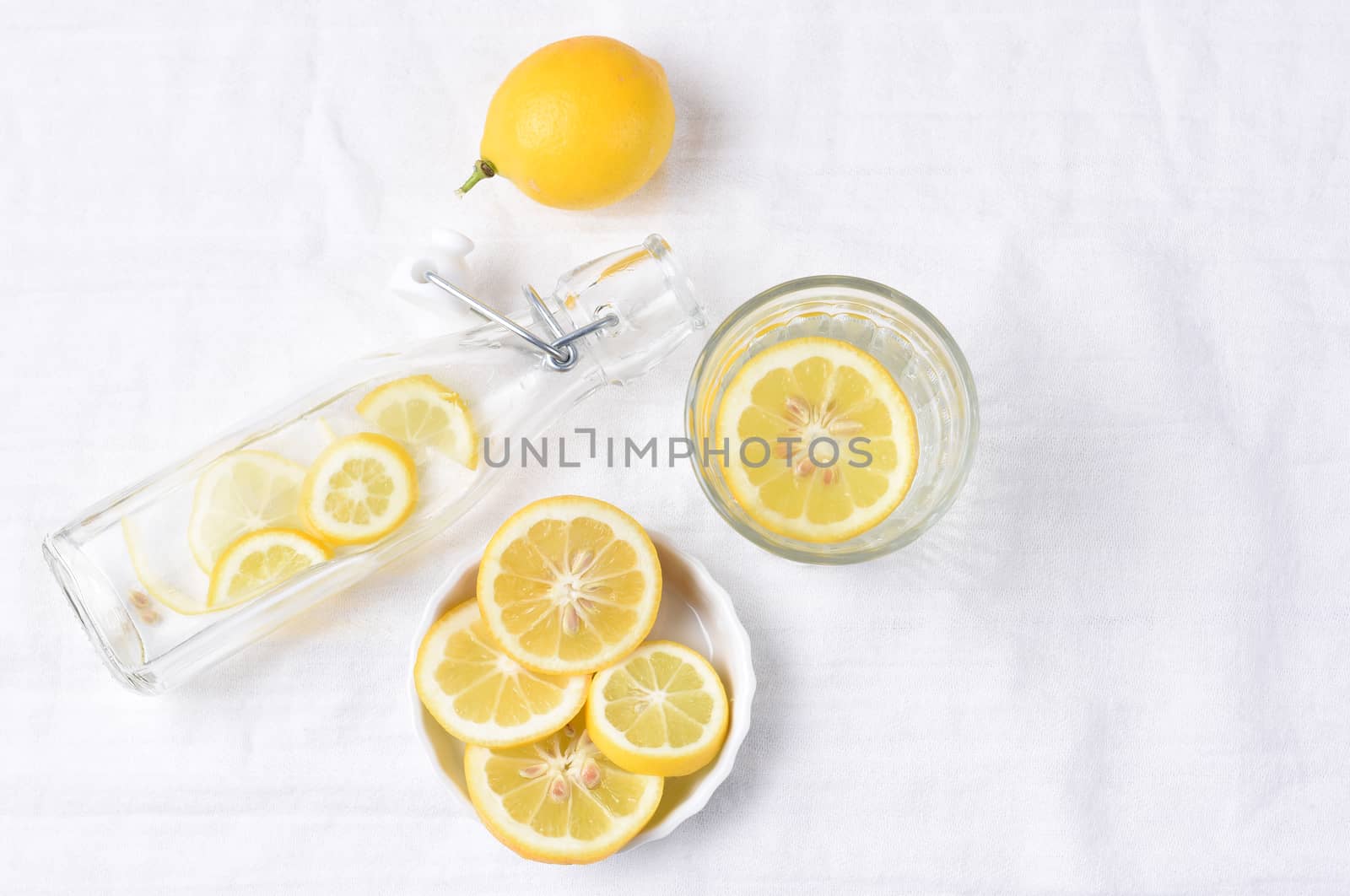 Top view of a glass of lemon water next to a swing bottle and whole piece of fruit. Horizontal format with copy space.