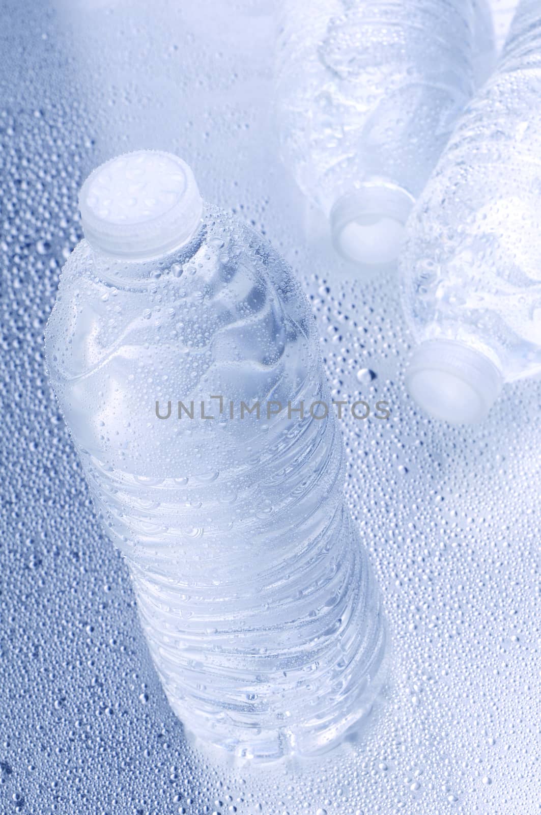 High angle shot with shallow depth of field of three water bottles on a wet surface. Vertical format with intentional cool tones.