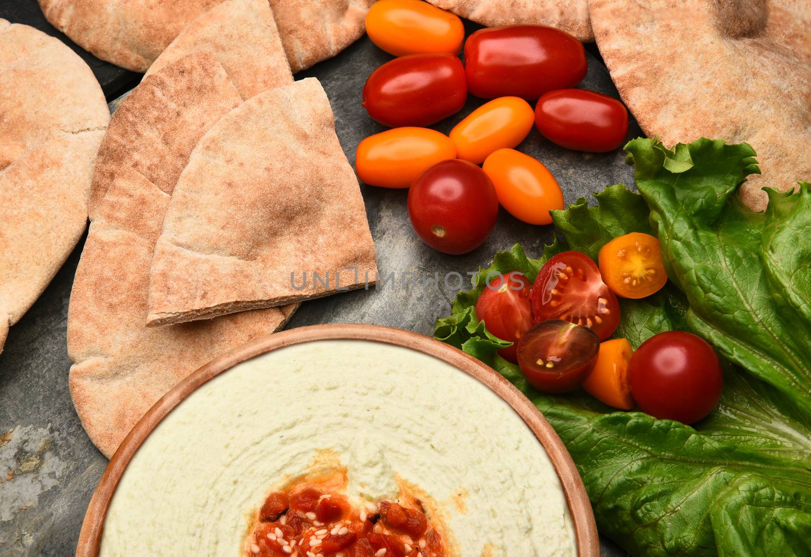 Top view of pita bread, edamame hummus, and medley tomatoes on a slate table. 