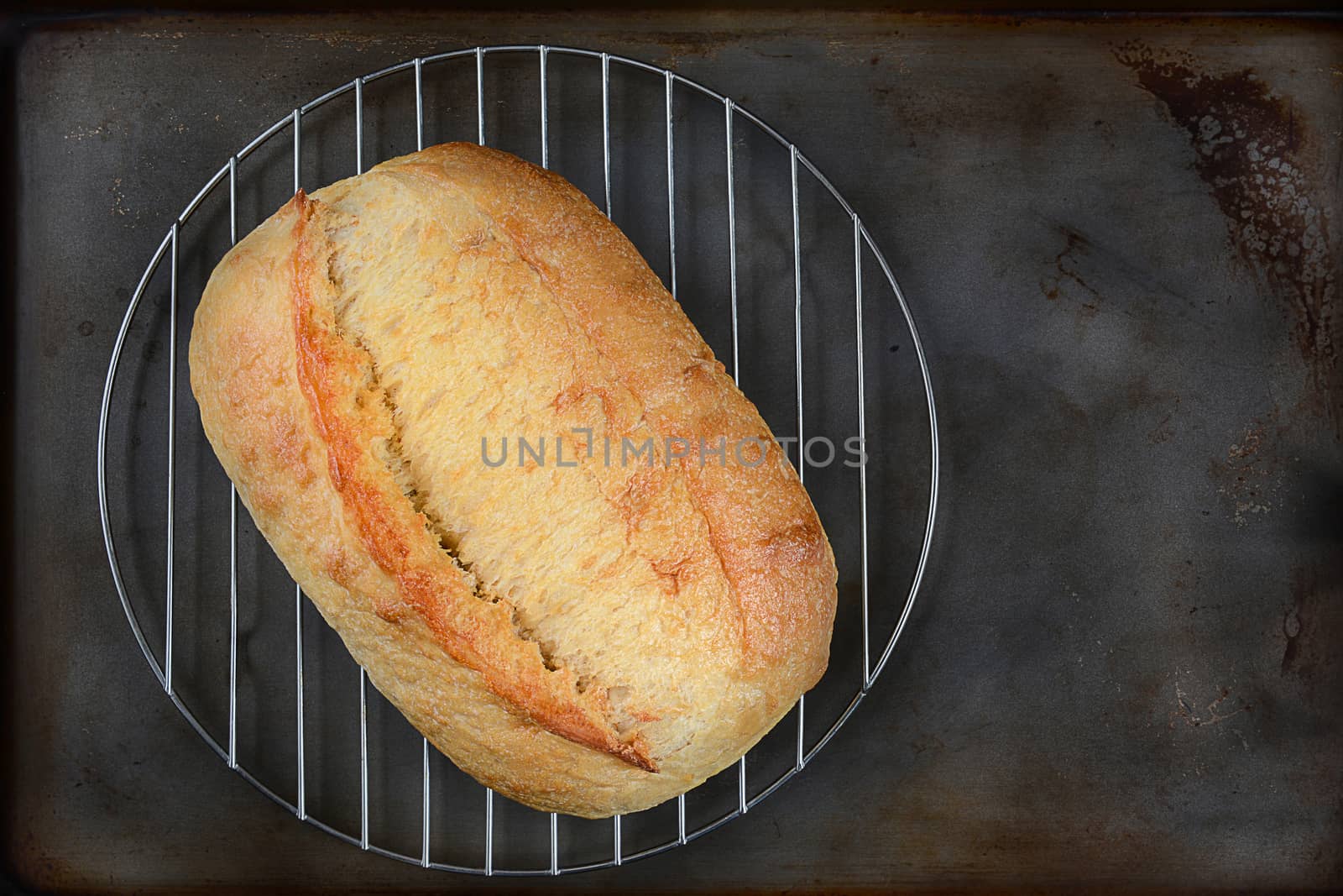 High angle shot of a fresh baked loaf of bread on a cooling rack. Horizontal format on a well used baking sheet.