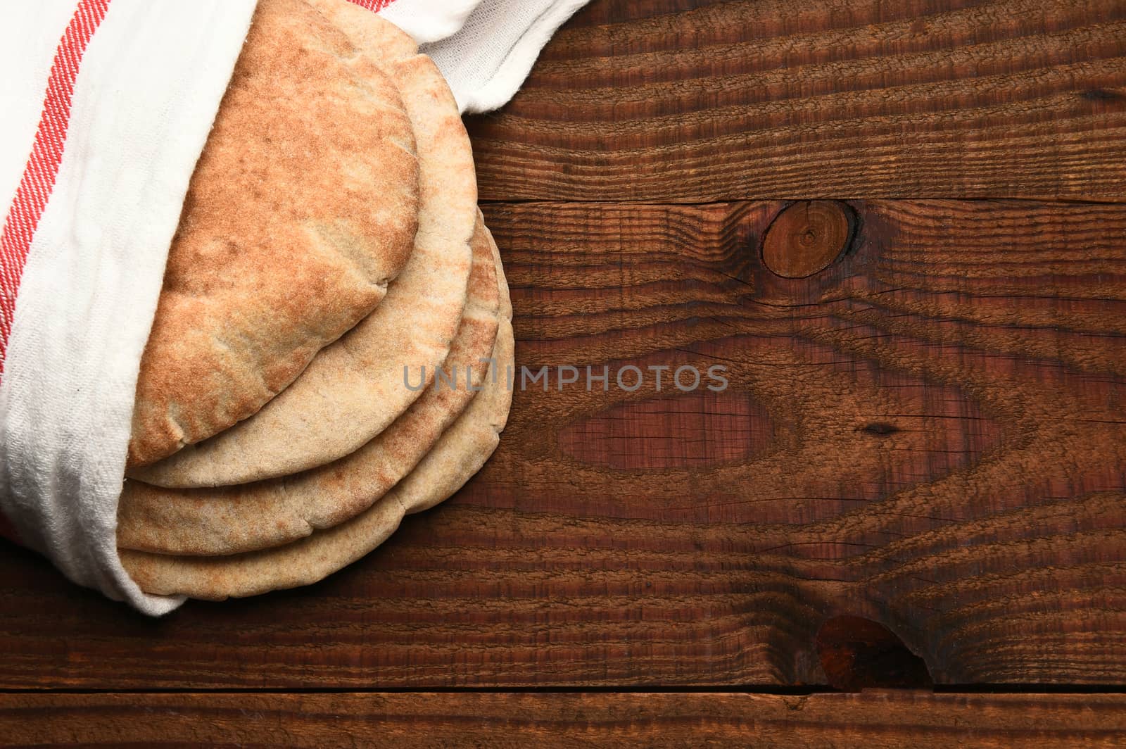 Whole wheat pita bread on a rustic wood table with copy space. The bread is wrapped in a towel and seen from a high angle.