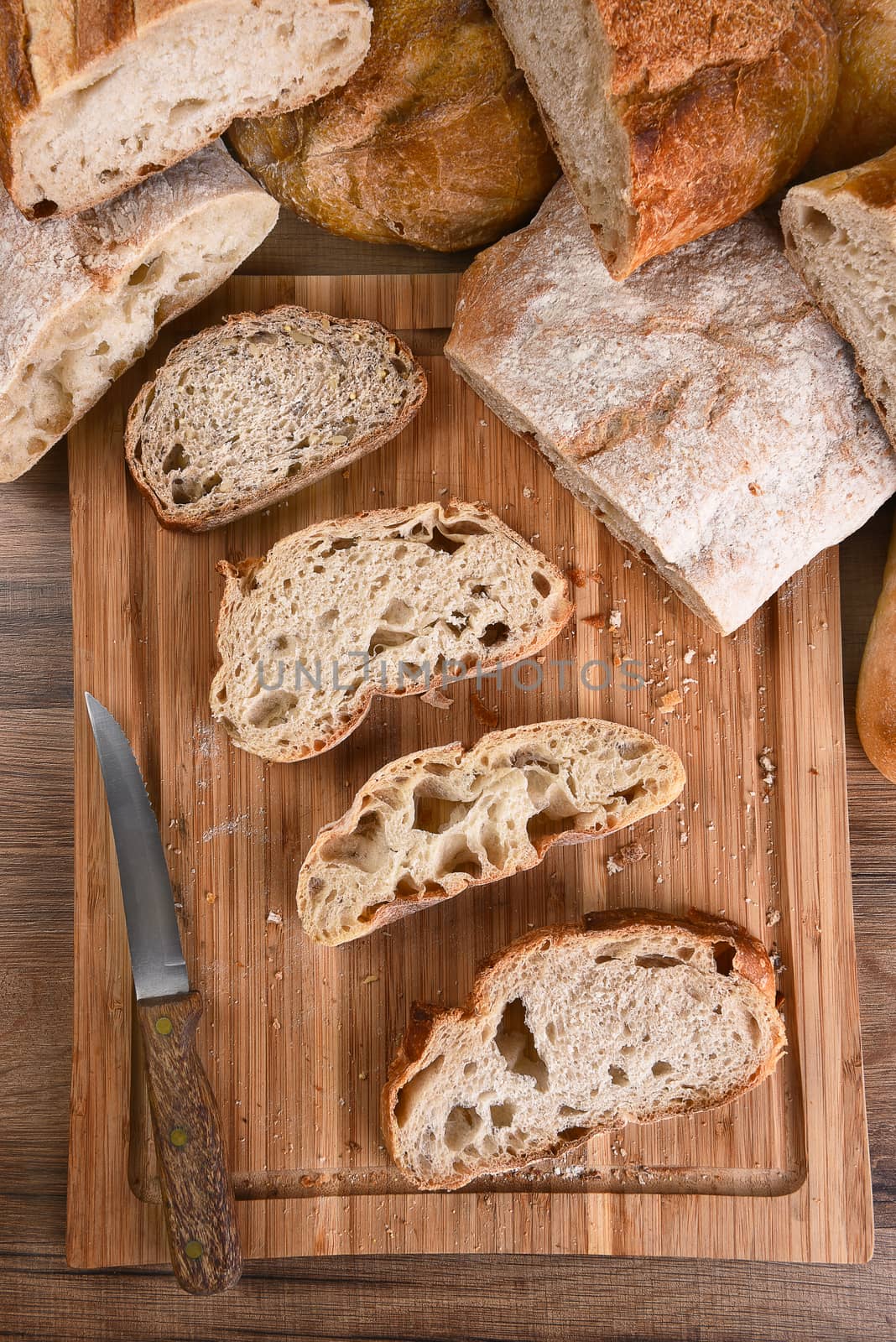 A variety of fresh baked loaves of bread, with slices on a wood cutting board. Top view in Vertical format.