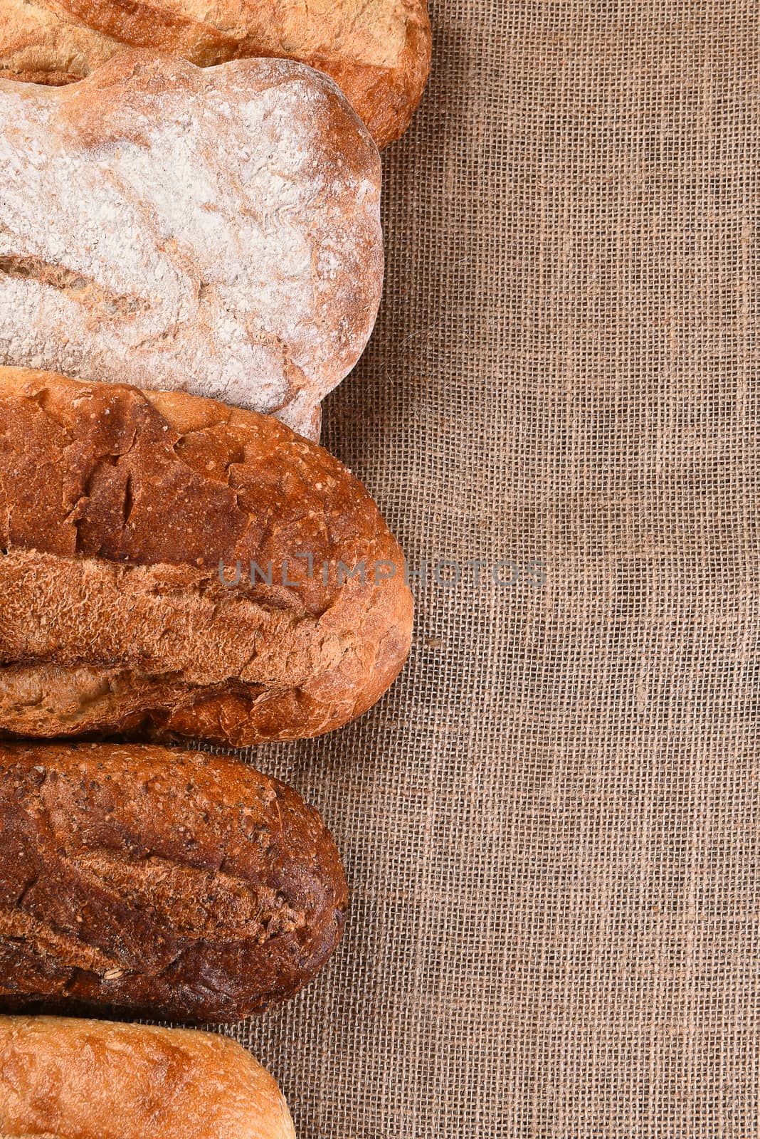 Five different loaves of bread on a wood table with copy space. Vertical format.