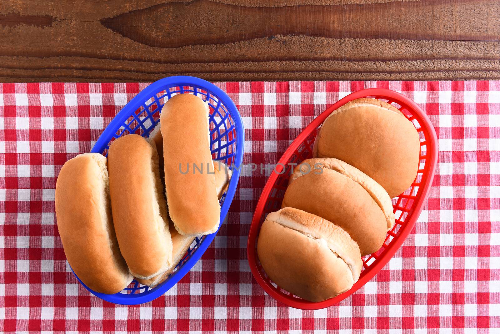 Hamburger and hot dog buns in plastic baskets on a picnic table . the red white and blue themed image is fit for patriotic holiday themes.