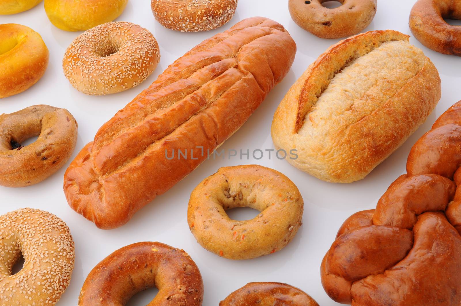 A large group of breads and bagels viewed for overhead on white with reflection. Items include: sesame seed bagels, french breaad, italian bread, baguette and more.Horizontal format that fills the frame.