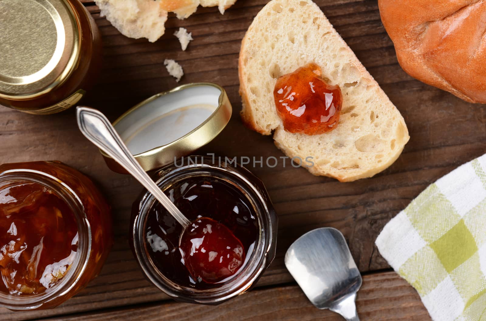 High angle shot of preserves and bread on a rustic wooden kitchen table. Horizontal format with selective focus.