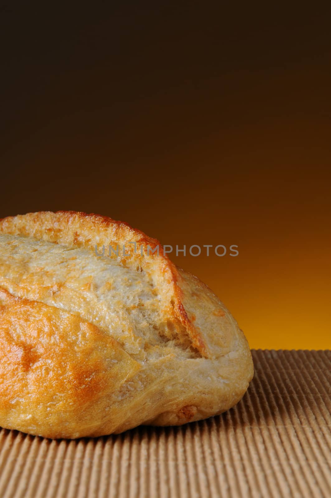 Closeup of a loaf of bread on a corrugated surface and a light to dark warm background.