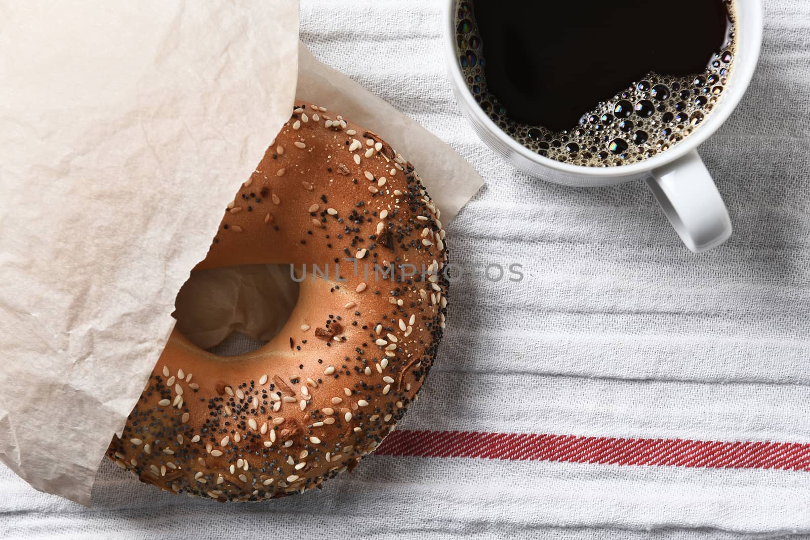 Fresh bagel and hot cup of coffee on a tea towel. High angle view in horizontal format.