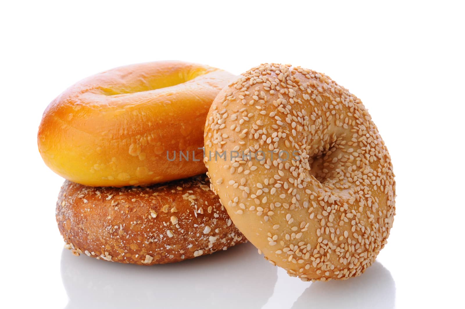 Three different bagels on a white surface with reflection. One each of an egg bagel, sesame seed, and mulit-grain Bagel are shown. 