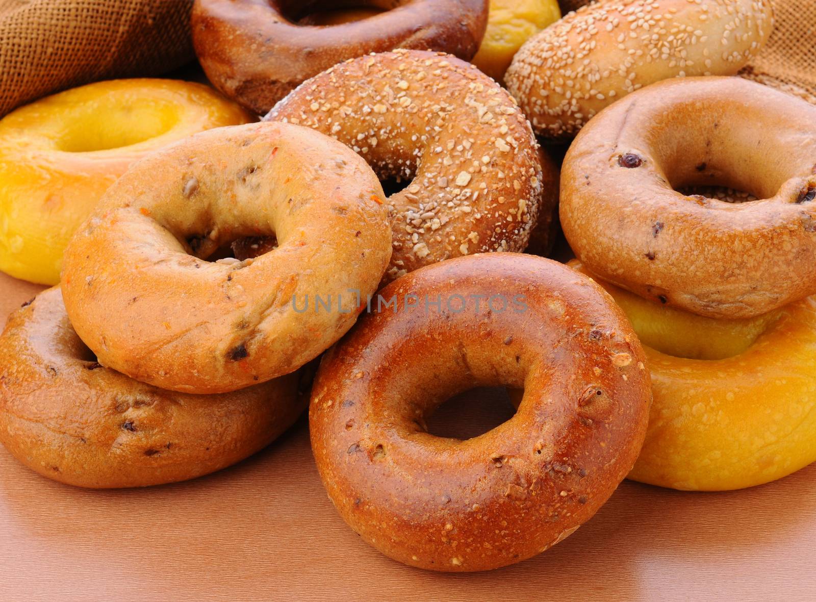 Closeup of a group of assorted bagels on a wood table top with burlap in the background. Bagels include, egg, whole grain, cinnamon raisin, sesame seed