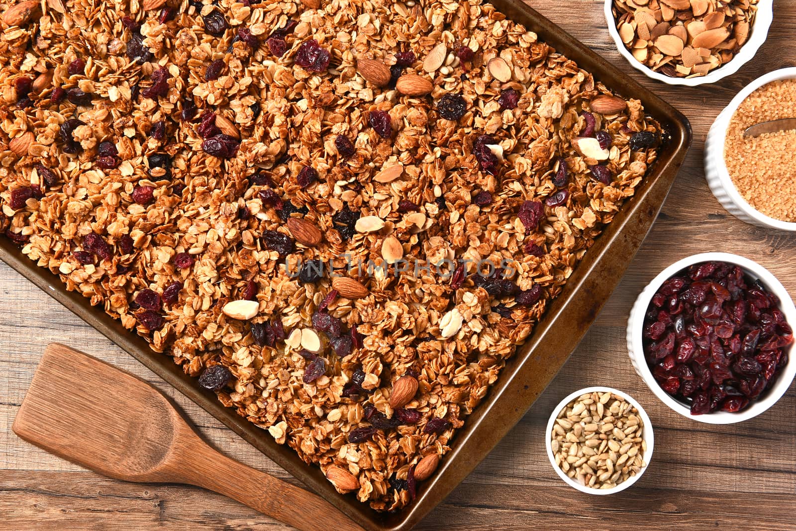 Horizontal overhead view of fresh homemade granola. Closeup of a baking sheet filled with the tasty, healthful food with containers of ingredients.