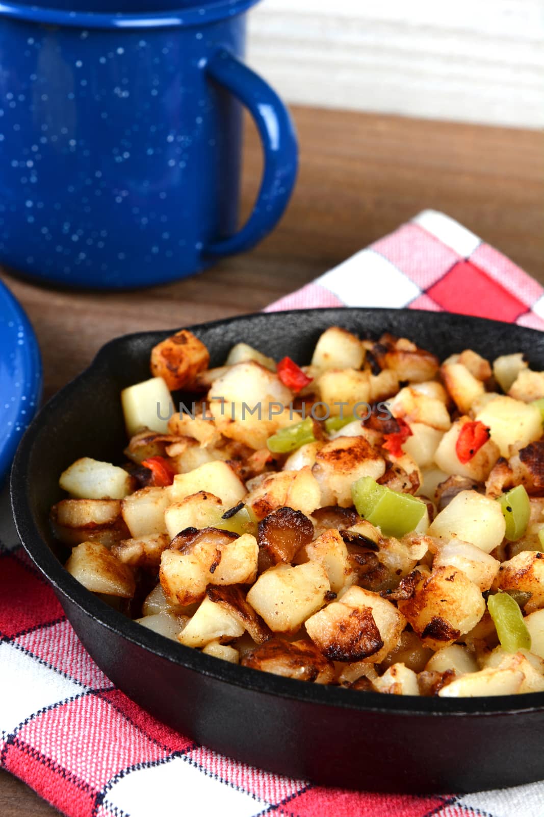 Closeup of a cast iron skillet full of breakfast potatoes. Vertical format with shallow depth of field.