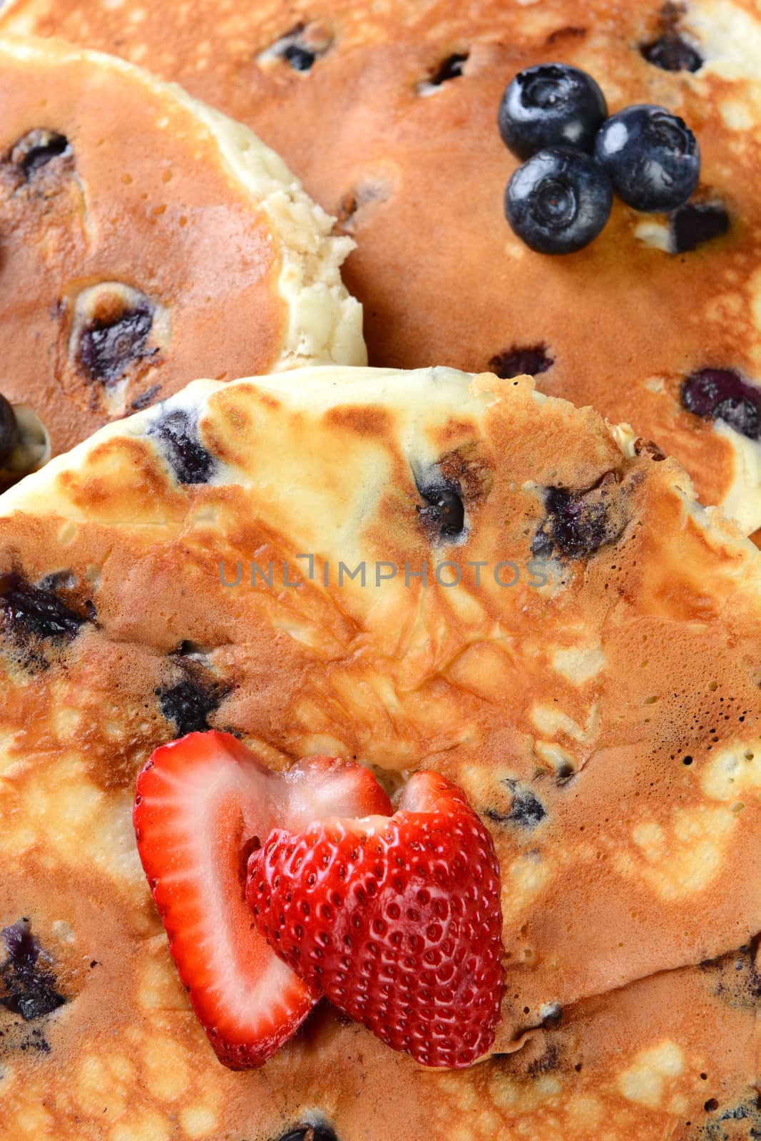 Overhead view of blueberry pancakes with a cut strawberry. 