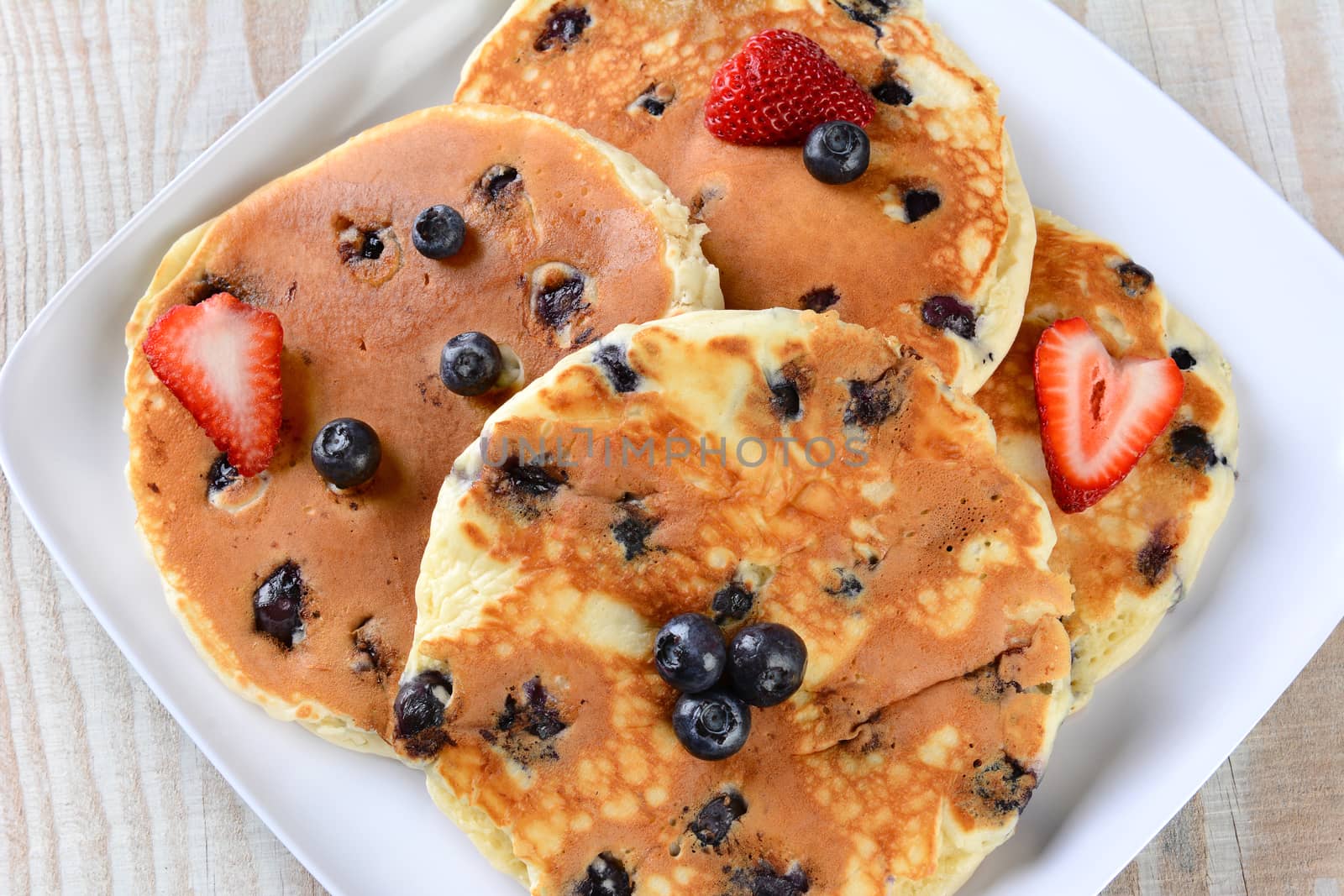 Overhead closeup view of a plate full of fresh homemade pancakes with blueberries and strawberries.