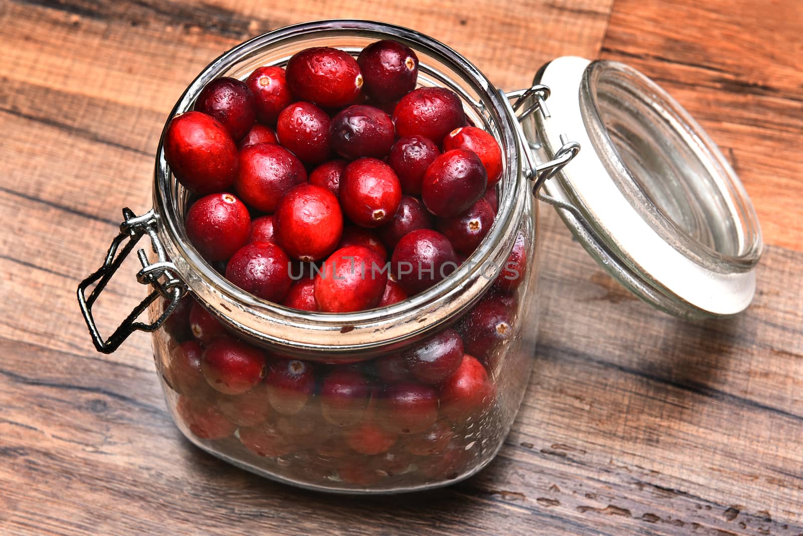 High angle closeup of a jar full of fresh whole cranberries on a rustic wood table.