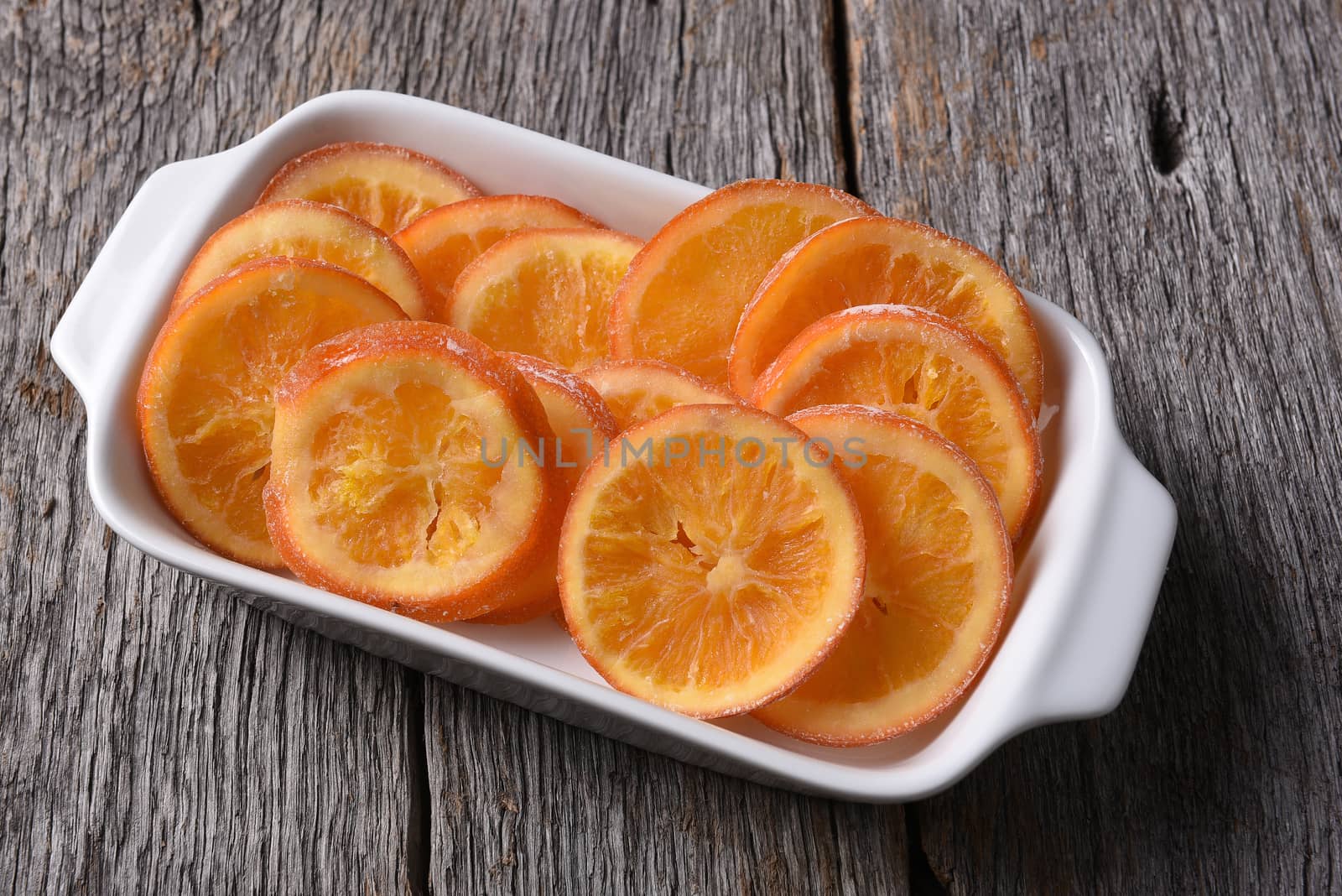 An rectangle serving plate of dried sweetened orange slices on a rustic wood surface. 