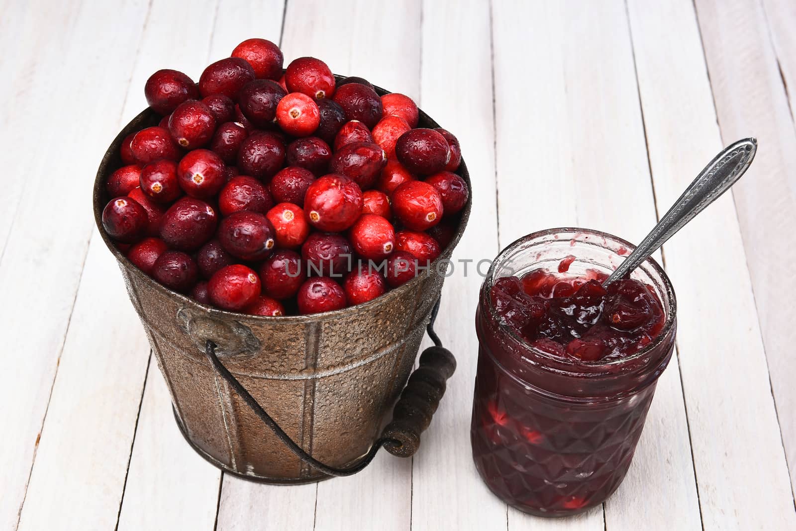 A bucket of fresh picked cranberries and a jar of sauce by sCukrov