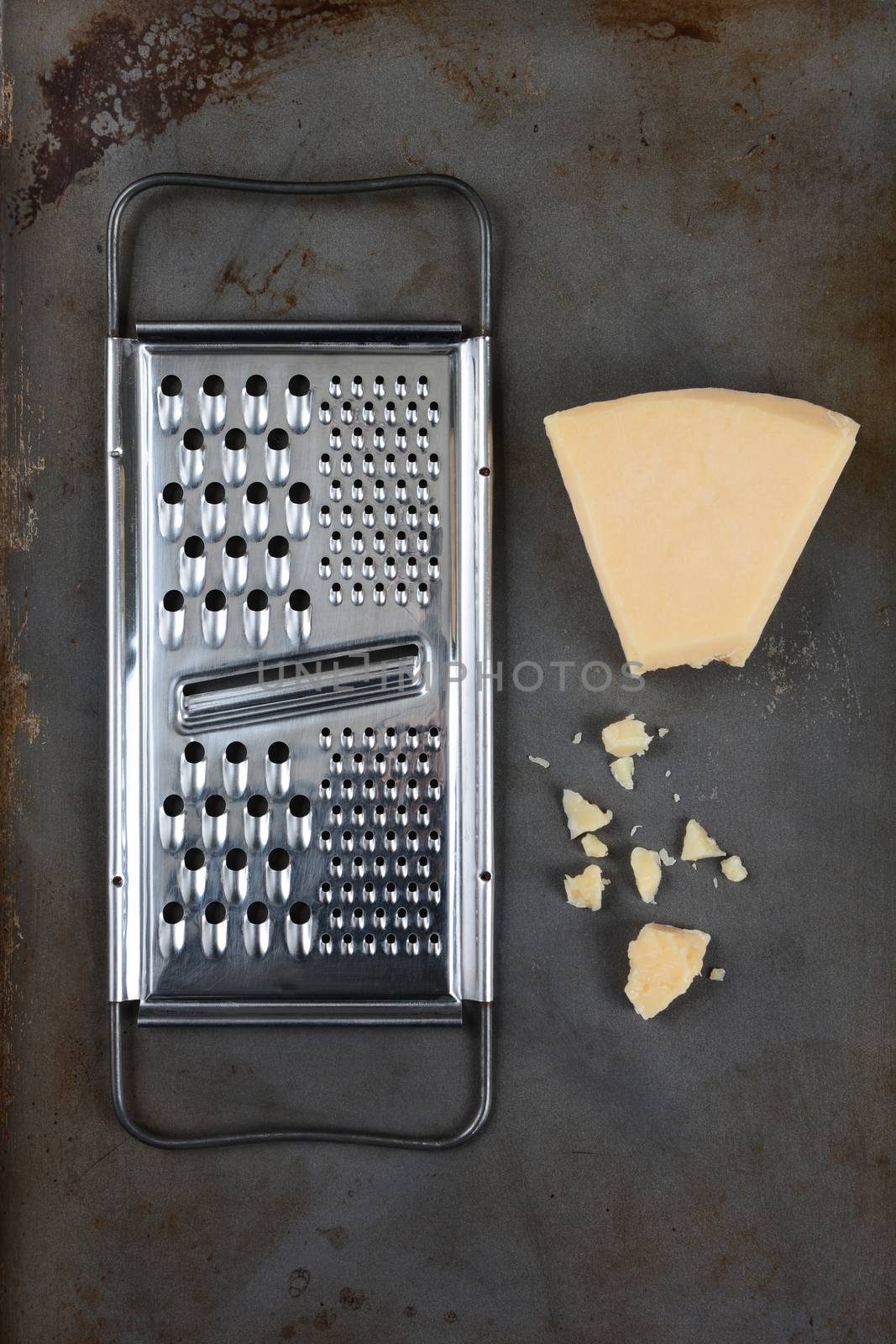 High angle shot of a broken wedge of Parmesan cheese and grater on used baking sheet. Vertical format.