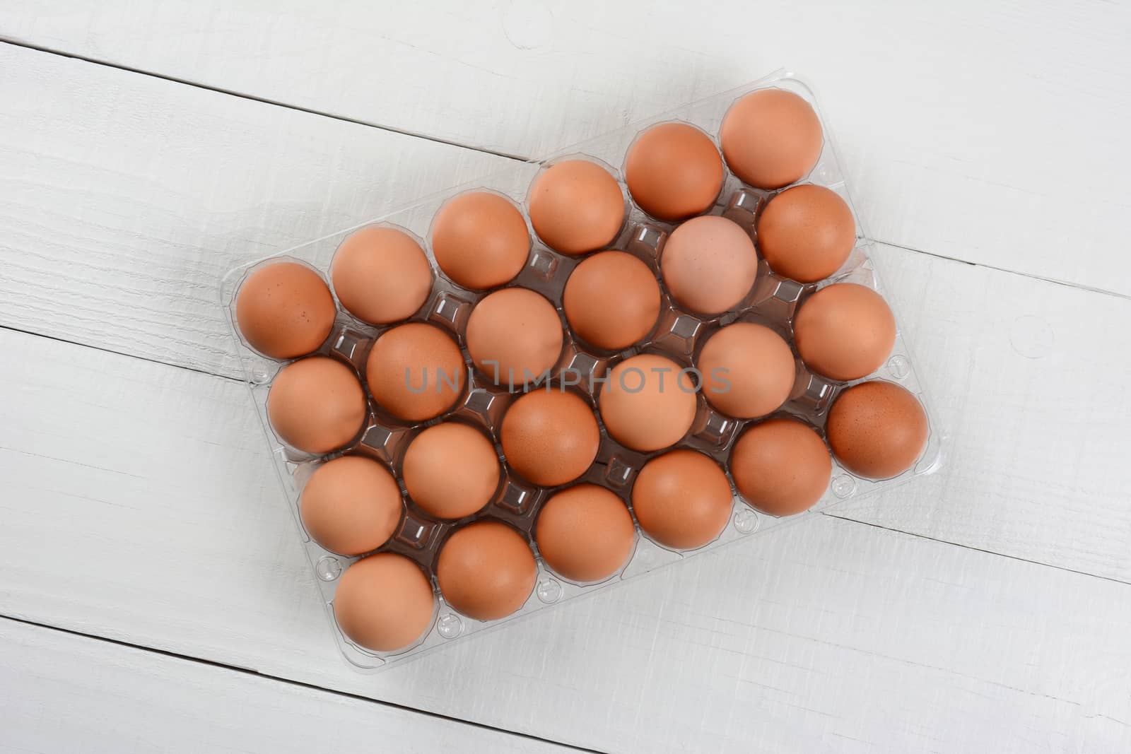 High angle shot of a 24 pack of organic brown eggs on a rustic white wood table. Horizontal format with copy space.