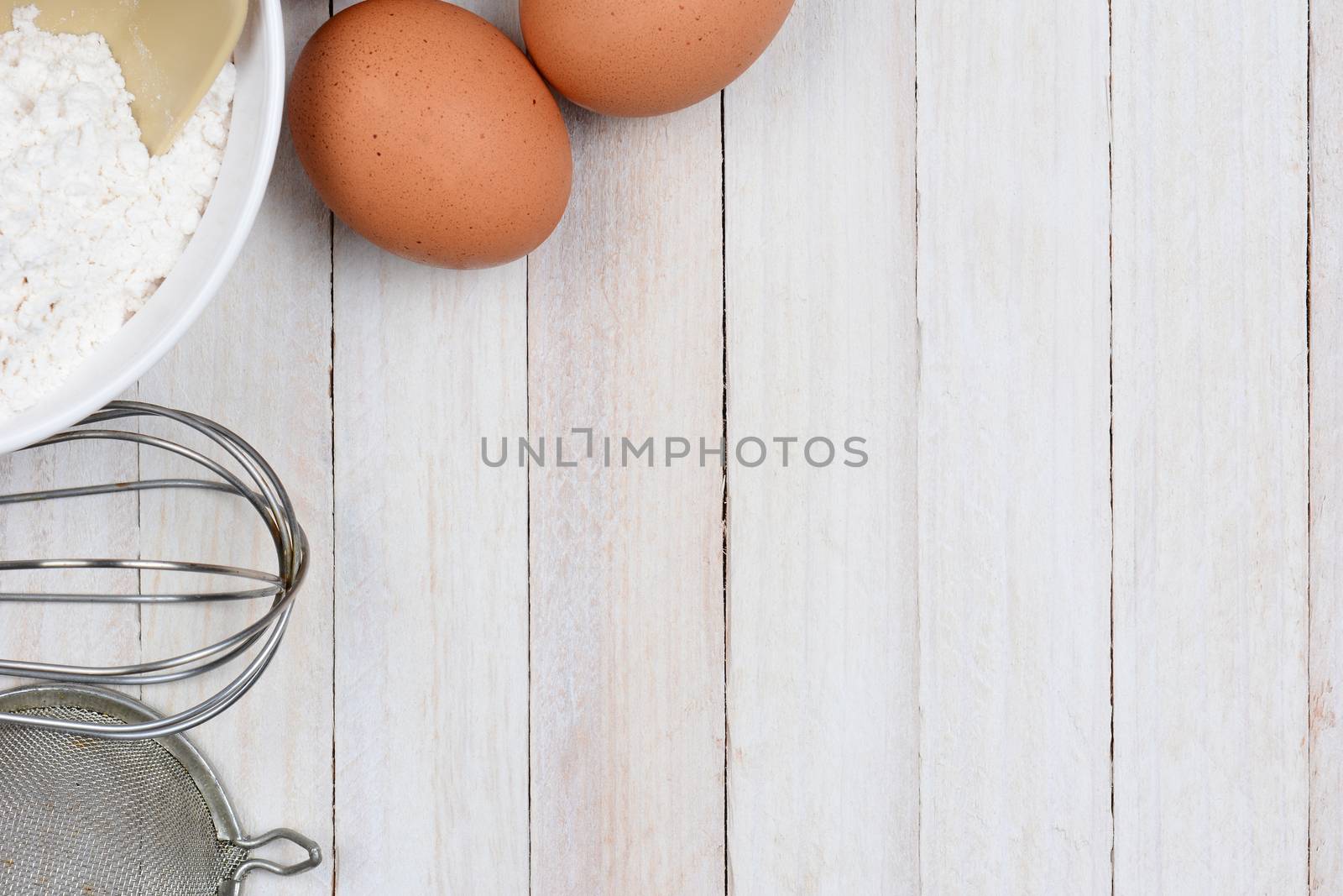 High angle shot of a baking still life, The objects, flour bowl, whisk, strainer and eggs are in the upper left corner, leaving plenty of copy space.