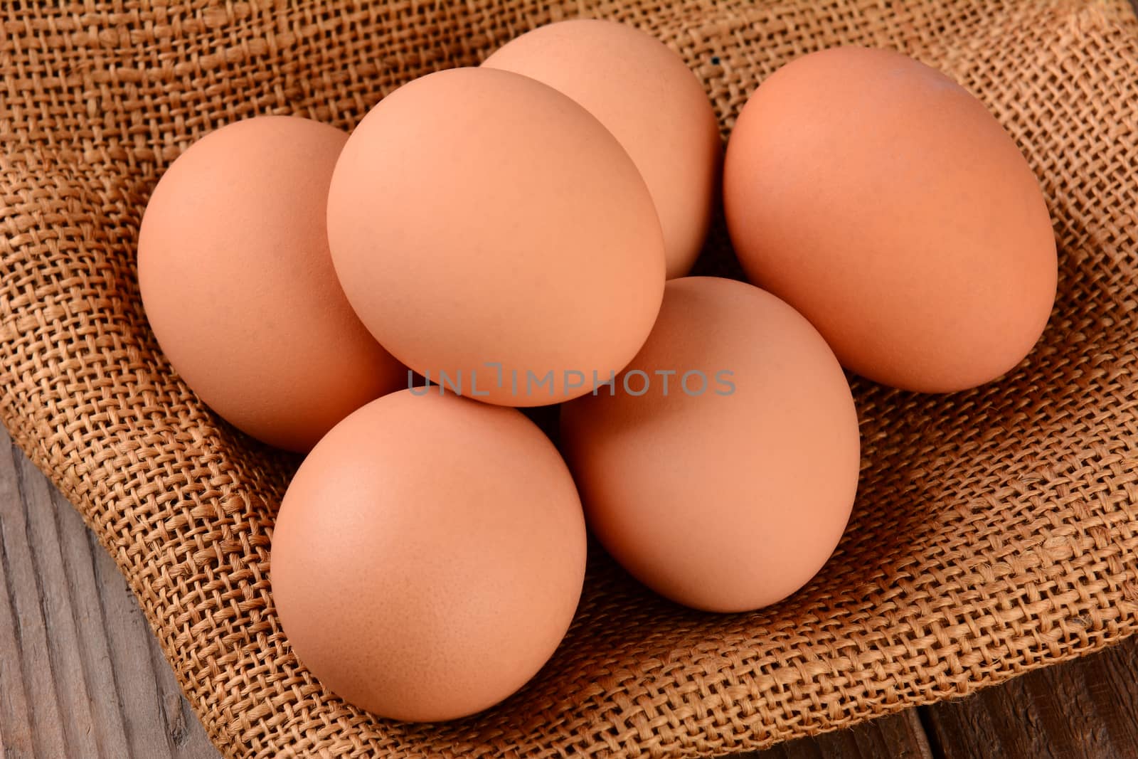 High angle shot of a group of brown eggs on a burlap sack. Horizontal format on a rustic wood surface.