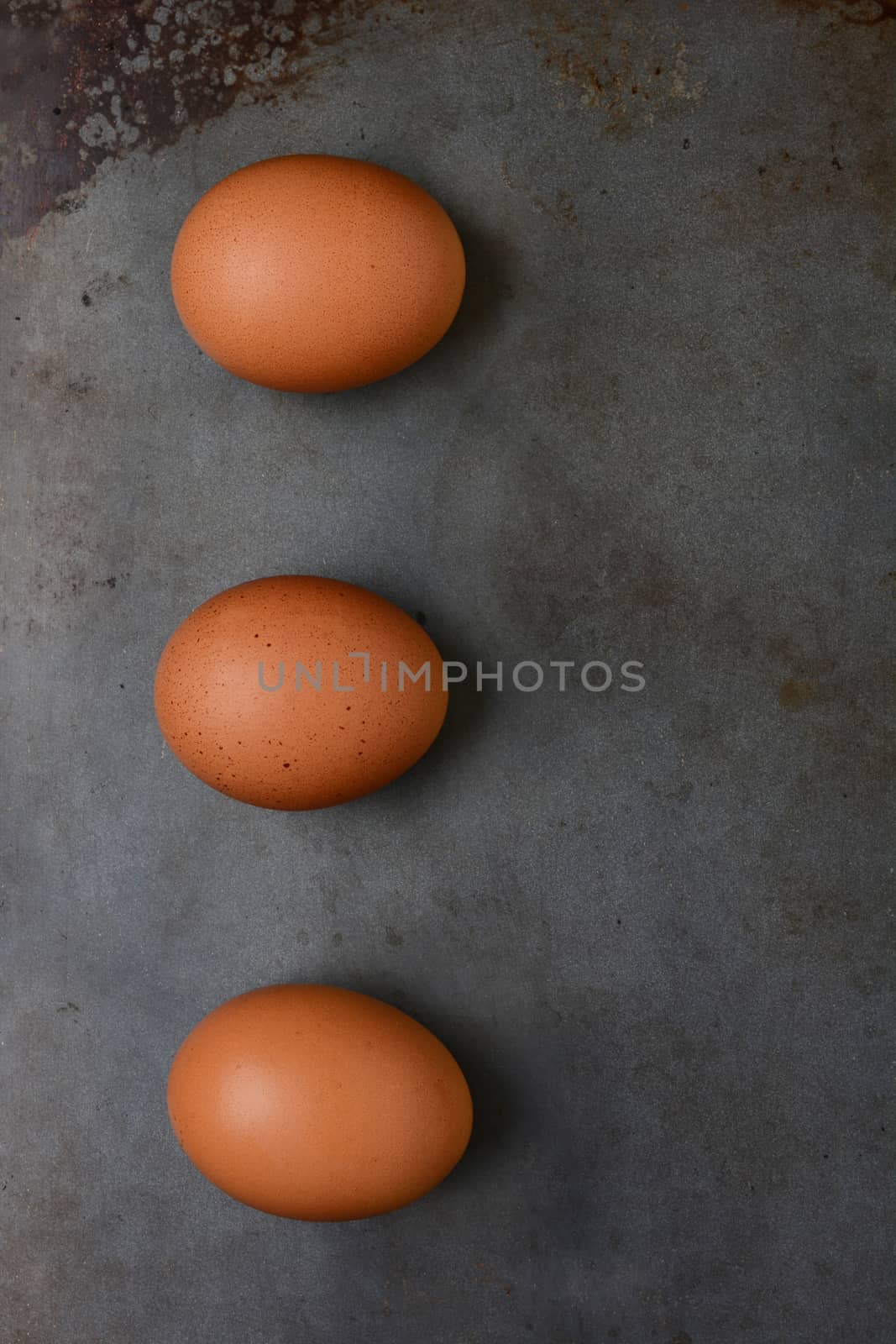 Overhead shot of three organic brown eggs on a metal baking sheet. Vertical format with copy space.