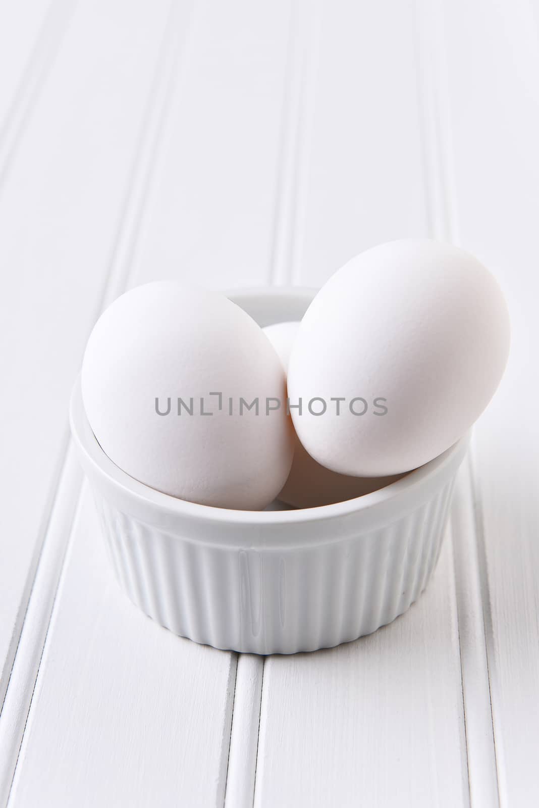 Egg White on White Still Life. Eggs in a ramekin on a white table. Vertical format with copy space.