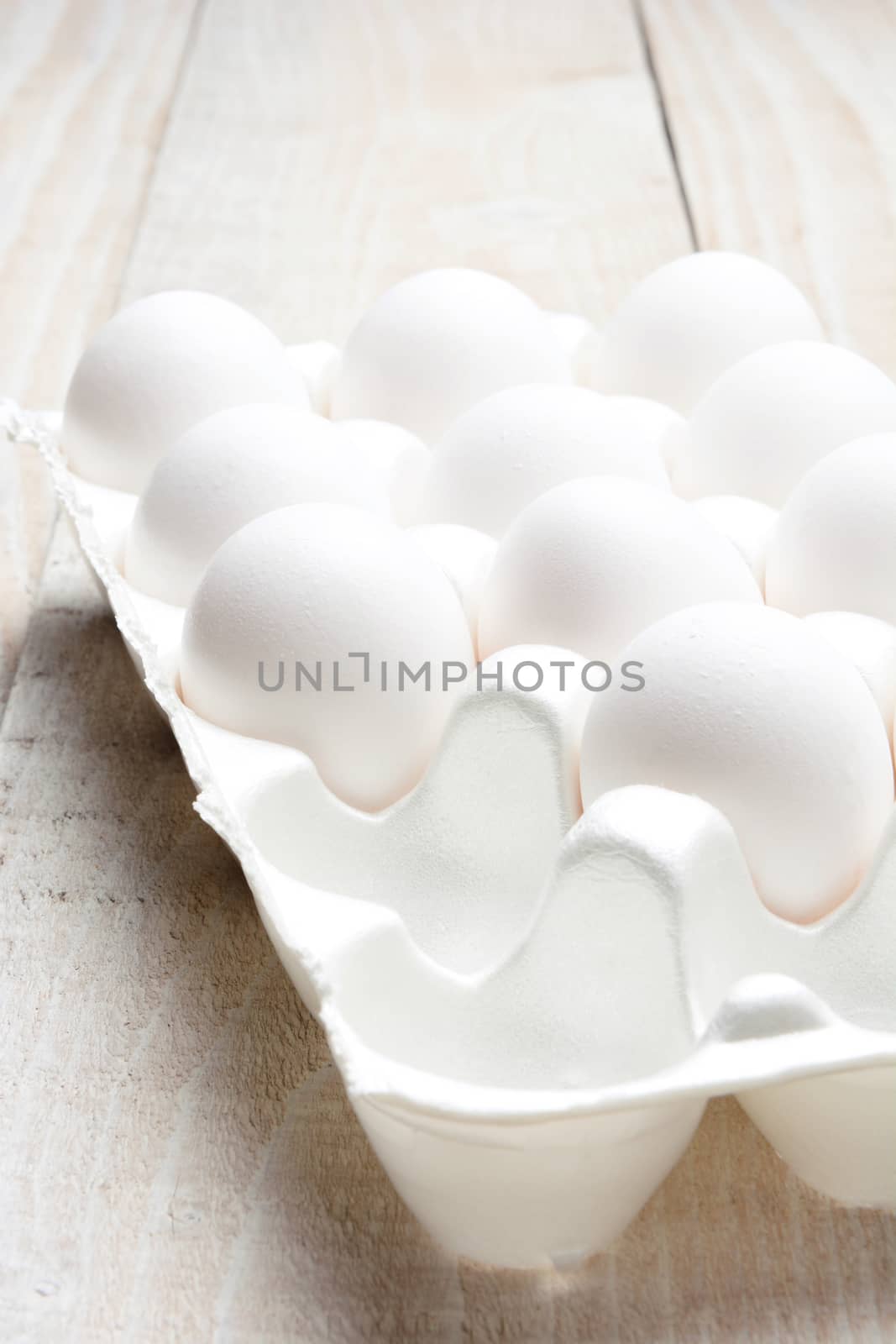 Closeup of a carton of eggs on white rustic wood table. Still life study of white on white.