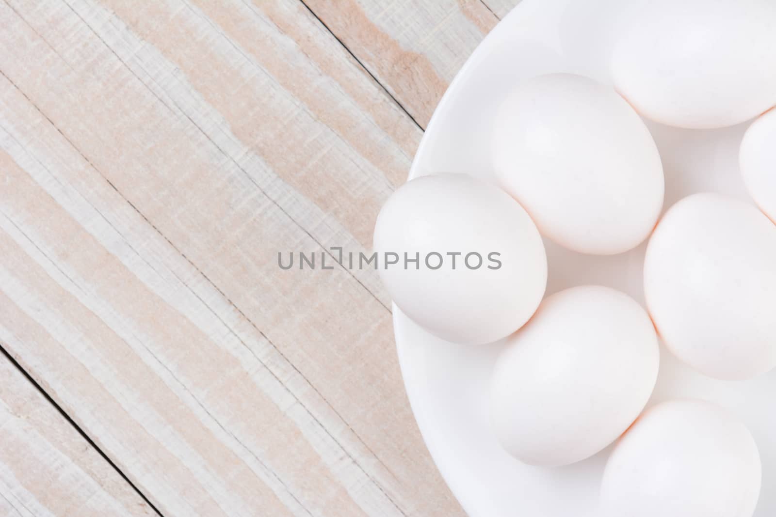 High angle view of a white bowl filled with white eggs on a white wooden rustic kitchen table. Horizontal format with copy space.