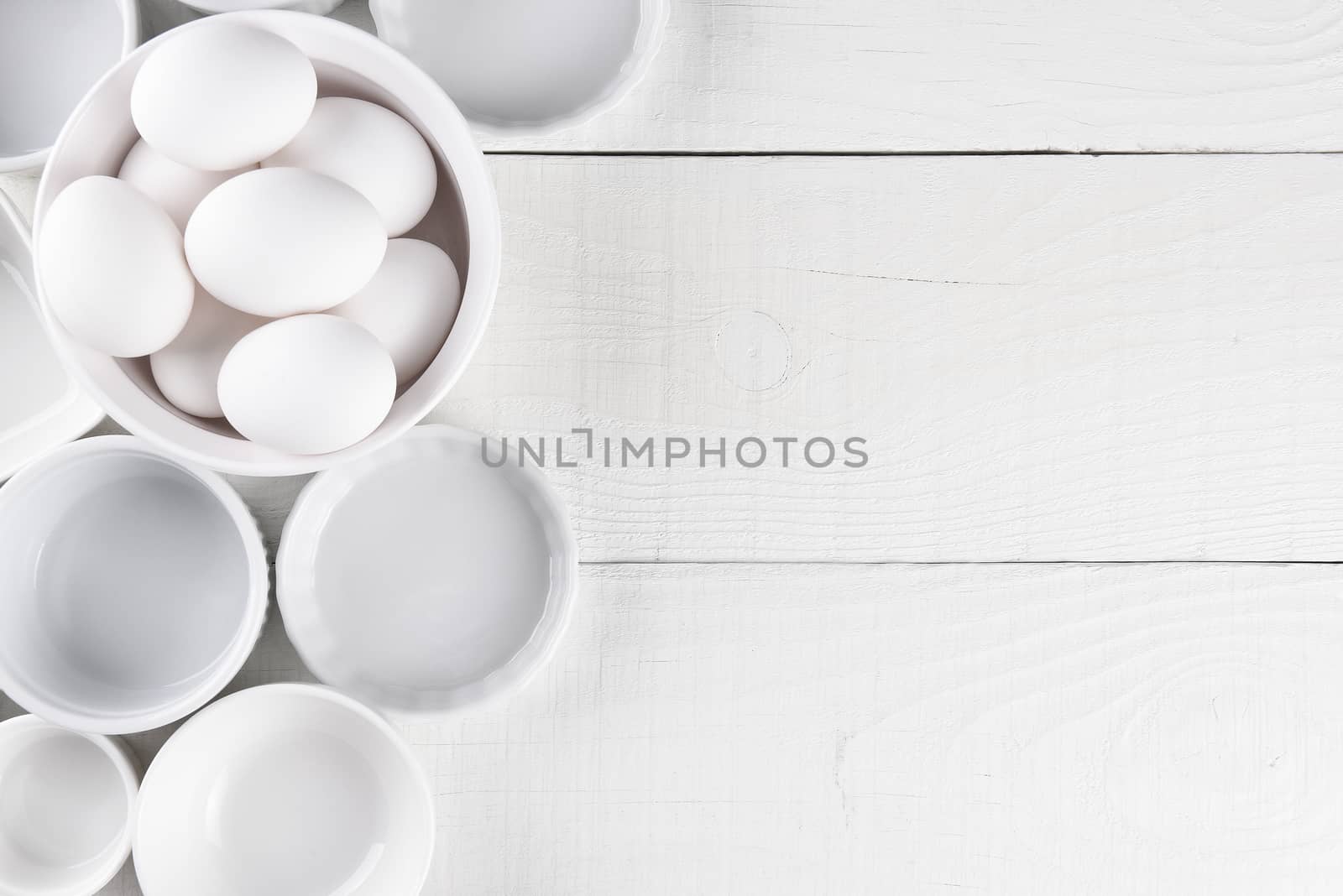 White Ramekins on White Wood Table with copy space. One dish is filled with eggs.