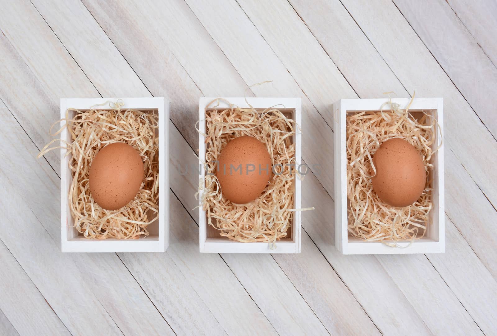 Three brown eggs in wood crates on a whitewashed wood surface. High angle shot in horizontal format. 