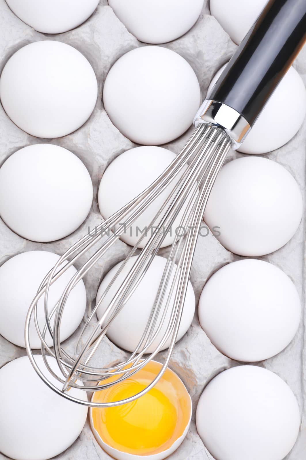 Closeup of a whisk laying across a carton of eggs, with one broken exposing the yolk. Vertical format filling the frame. This image can be easily rotated to a horizontal orientation to fit your layout.