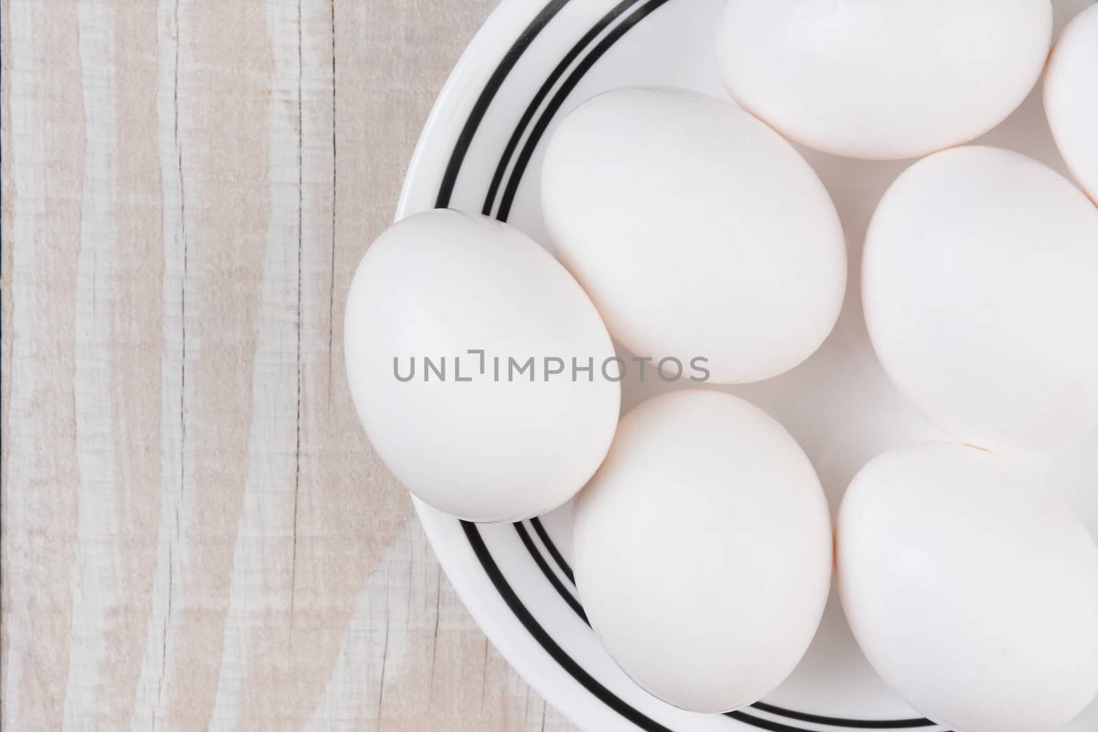 White eggs on a white plate with black trim on a rustic whitewashed table. Horizontal format with copy space.