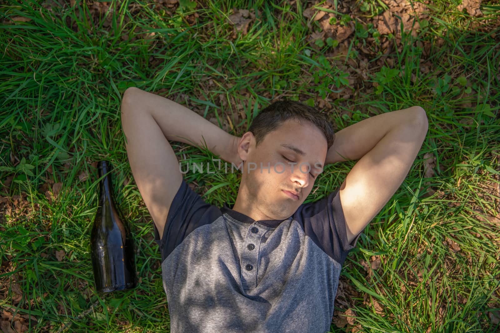 drunk man sleeping on a green field after using alcohol, a bottle lying next to a man by Edophoto