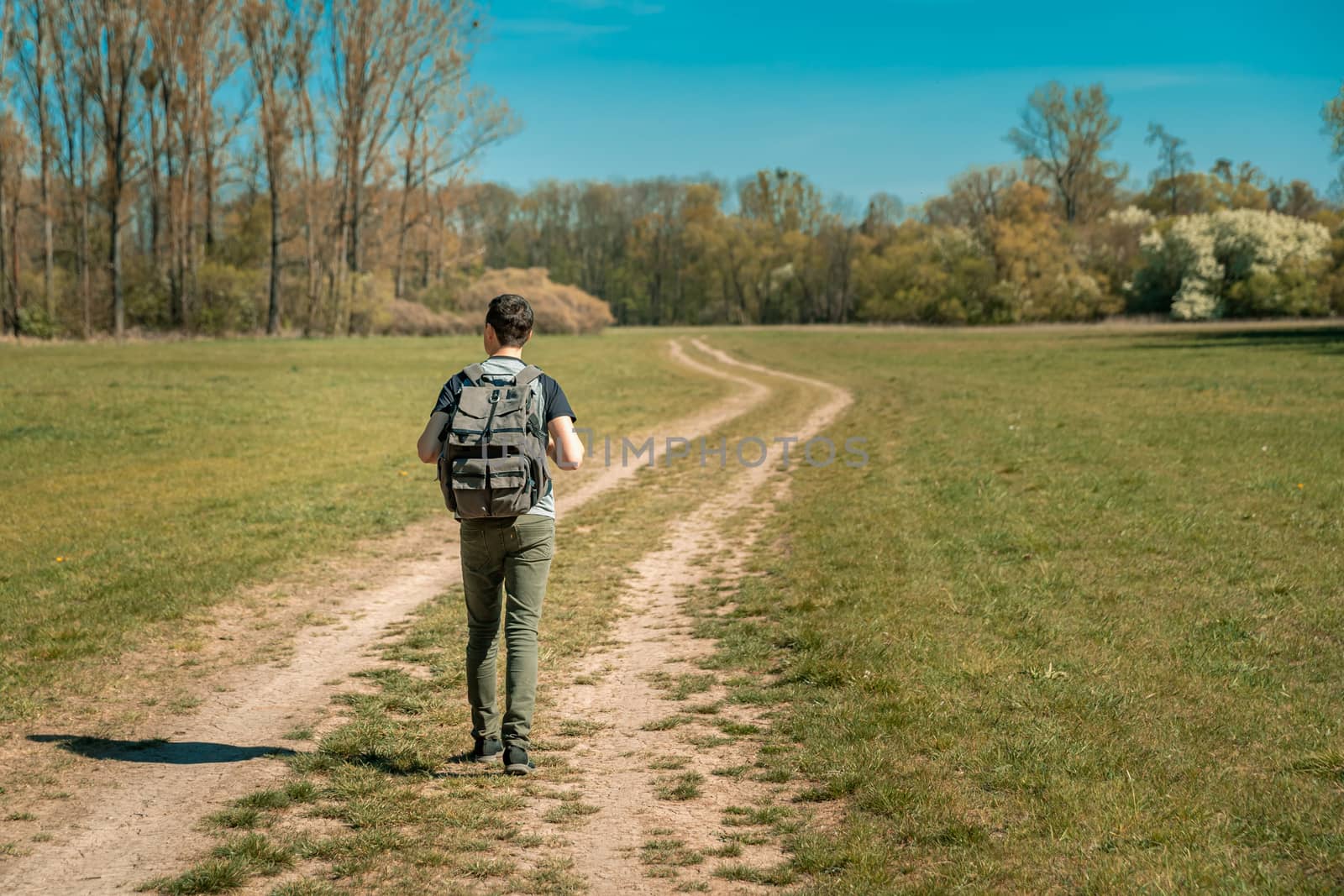 a hiker on a hike with a backpack on his back walks a dirt road towards the forest by Edophoto