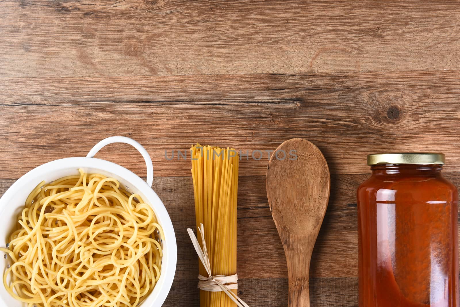 Italian Cooking Still Life with copy space. Woden spoon, dry spaghetti, cooked pasta and a jar of sauce on a wood kitchen table.