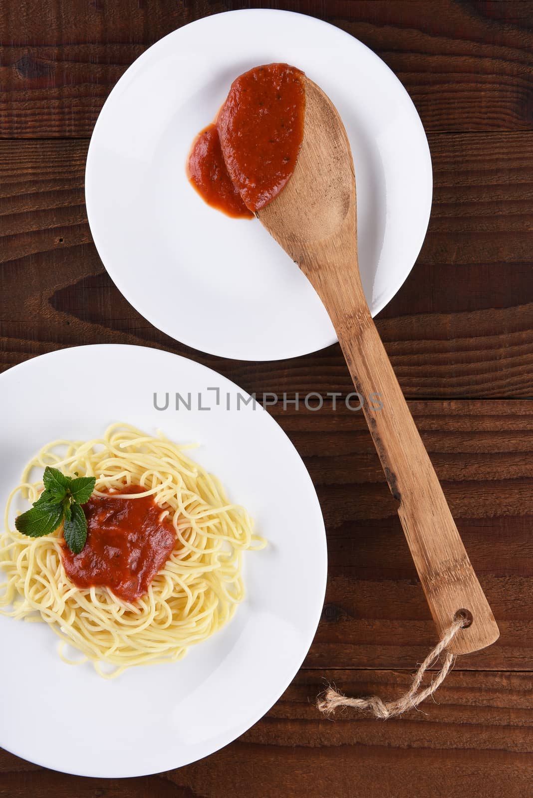 High angle view of a plate of spaghetti with marinara sauce and garnish. A second plate with a wood spoon and sauce in vertical format.