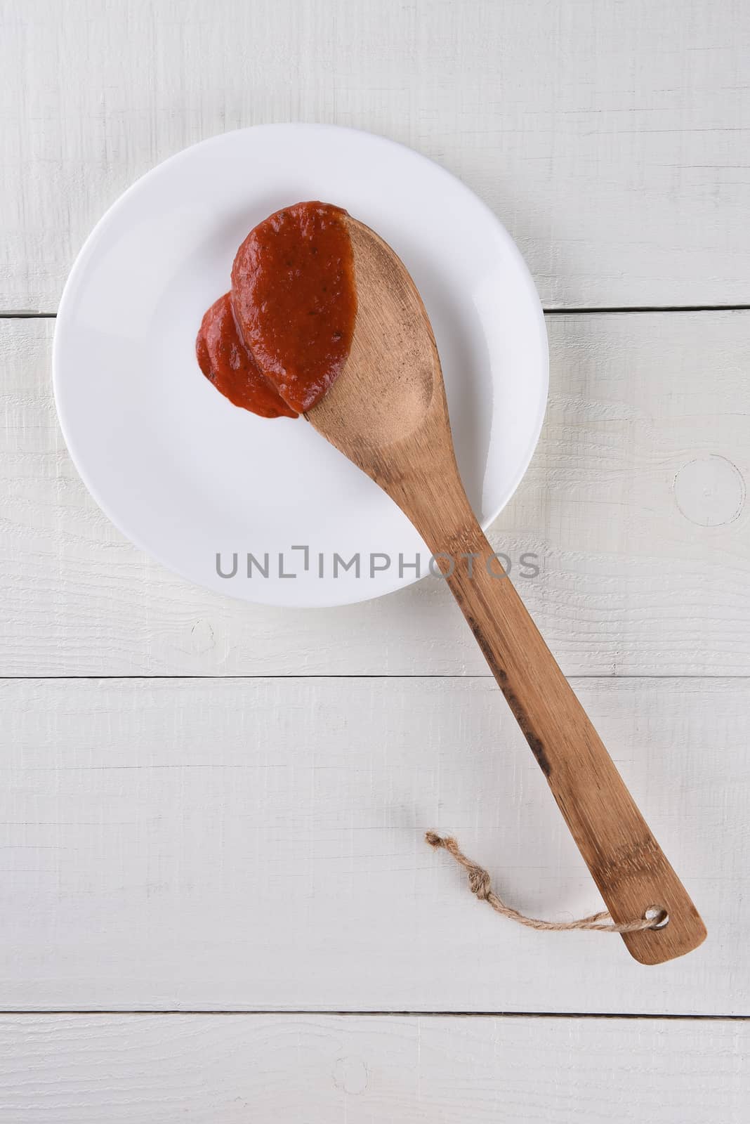 Top view of a wood spoon resting on a white plate with pasta sauce.