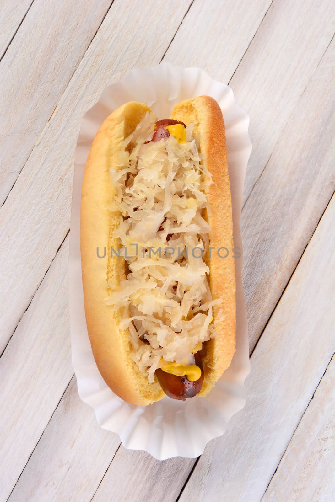 High angle shot of a Kraut Dog. A grilled hot dog on a bun with mustard and sauerkraut on a rustic white wood picnic table. 