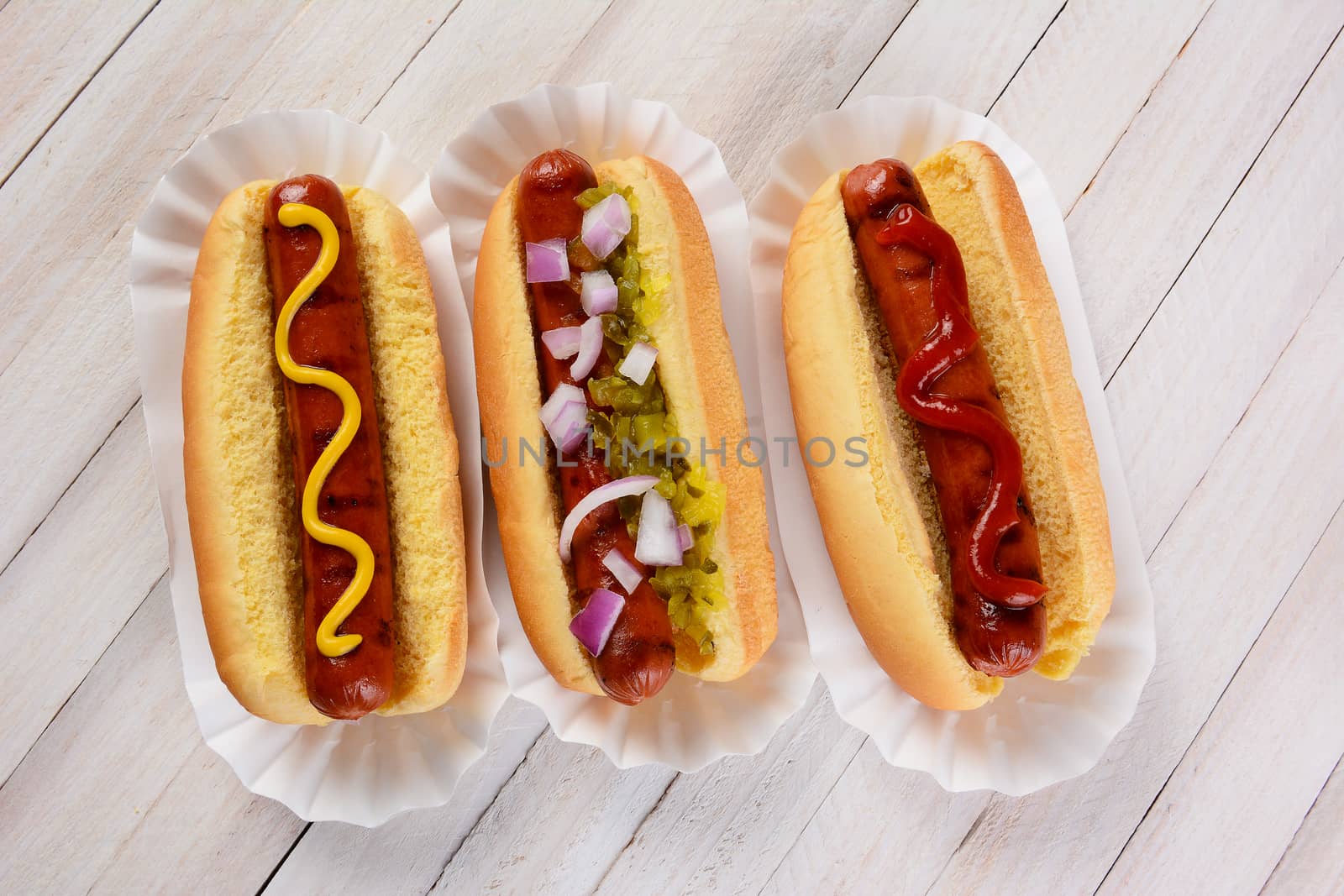 Top view of three hot dogs on a wood table with different condiments.