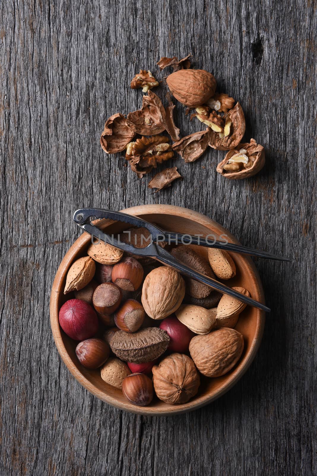 Overhead view of a bowl of mixed nuts with nutcracker and cracked nuts on a rustic wood table.