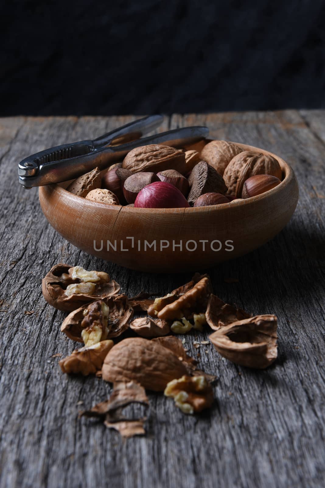 Vertical high angle shot of a bowl of mixed nuts with cracked walnuts in the foreground. 