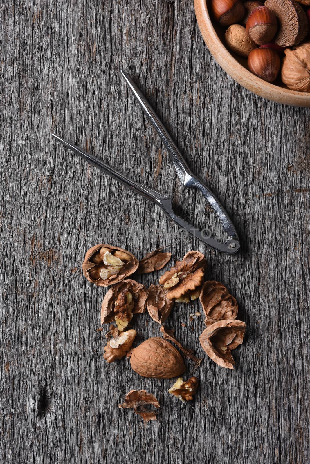 Top view of cracked walnuts nutcracker with bowl of mixed nuts in corner.