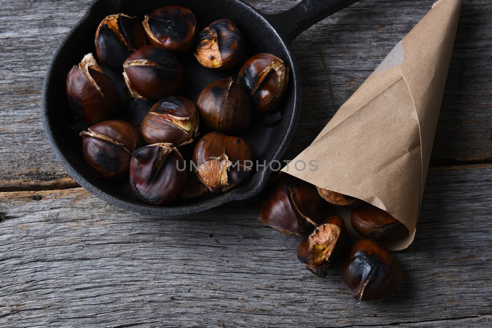 Roasted chestnuts in pan and a paper sack full of cooked nuts.